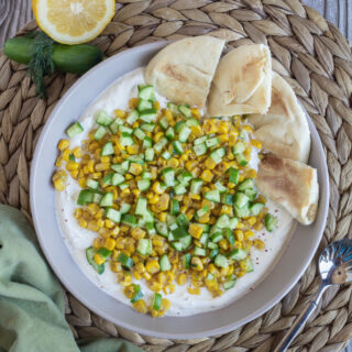 Sautéed Corn with Cucumbers over Lemon Dill Labneh, a creamy spread topped with seasonal vegetables, served with naan wedges.