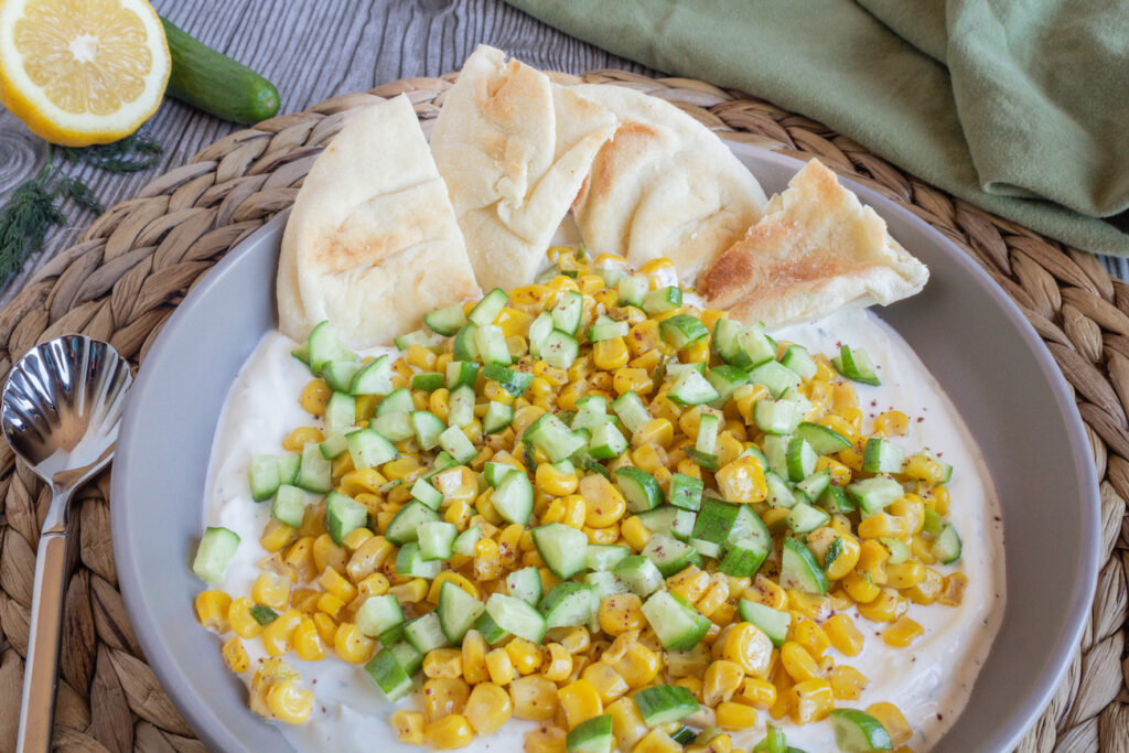 Sautéed Corn with Cucumbers over Lemon Dill Labneh, a creamy spread topped with flavorful veggies and served with naan wedges.